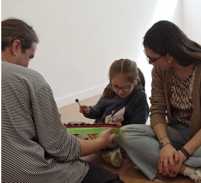 Alumna toca el xilófono con unas baquetas, con varias profesionales.