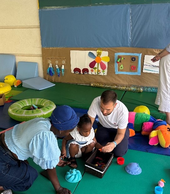 Dos adultos interactúan con una niña pequeña en la zona de  estimulación para niños pequeños