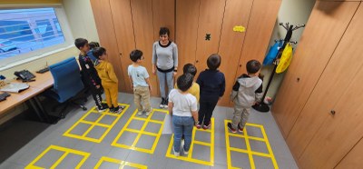 Alumnos sobre cajetines braille colocados en el suelo, simulan la palabra “casa” en braille.