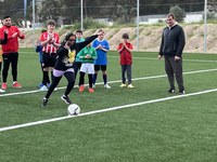 niña lanzando un penalti a portería mientras sus compañeros y entrenador la animan