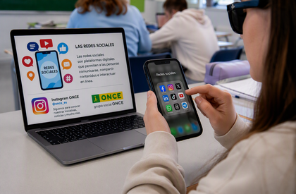 Imagen de un aula con varias personas trabajando. En primer plano, una persona sostiene un teléfono móvil con iconos de redes sociales. A la izquierda hay un ordenador portátil con una diapositiva titulada “LAS REDES SOCIALES”, que incluye texto explicativo y gráficos. En la parte inferior de la pantalla aparece el perfil “Instagram ONCE @once_es” junto al logotipo de la ONCE. La mesa está despejada, sin cuaderno ni bolígrafo, y al fondo se ven más personas y mobiliario de clase desenfocados.