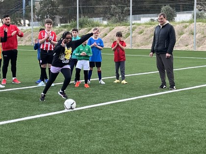 niña lanzando un penalti a portería mientras sus compañeros y entrenador la animan