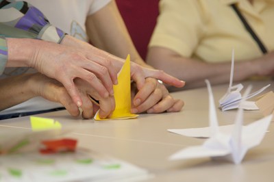 Se observan las manos de una persona realizando figuras de papel con ayuda de otra persona