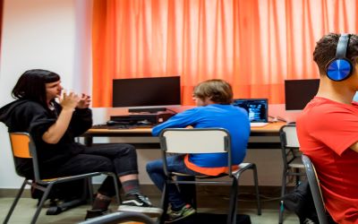 Aula de informática con alumnado donde hay una intérprete explicando algo a uno de los alumnos