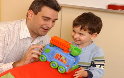 Niño jugando con un camión de juguete junto a su padre